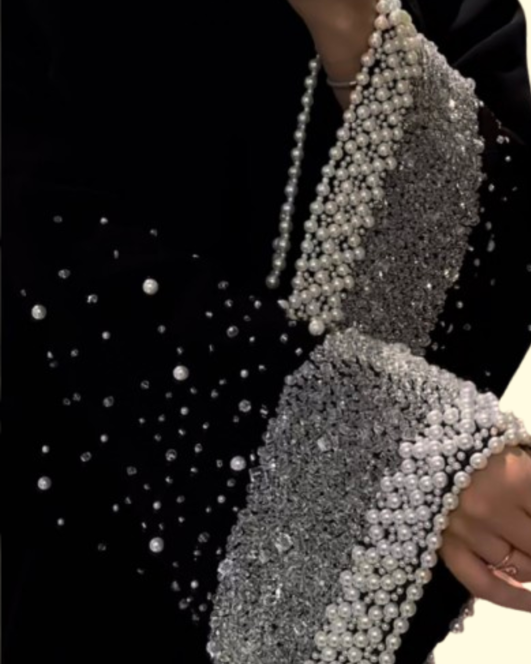 Close-up of a black abaya sleeve adorned with silver beads and white pearls in an intricate design.