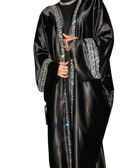 A woman in a black, high-shine satin abaya featuring heavy silver rhinestone and crystal embellishment along the front edges and wide cuffs