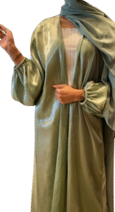 A woman in a flowing, shimmering sage green abaya with voluminous balloon sleeves, worn open over a white ribbed top and paired with a matching green hijab.