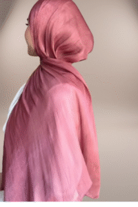 wearing a shimmery, dusty rose-colored hijab against a soft, neutral, light