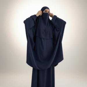 Woman wearing a navy blue niqab and abaya, adjusting the face covering in a minimalist studio setting.