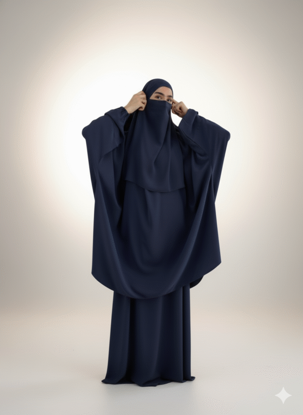 Woman wearing a navy blue niqab and abaya, adjusting the face covering in a minimalist studio setting.