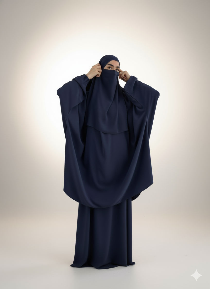 Woman wearing a navy blue niqab and abaya, adjusting the face covering in a minimalist studio setting.