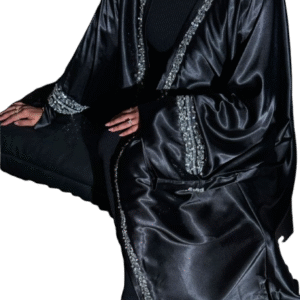 A woman in a black, high-shine satin abaya featuring heavy silver rhinestone and crystal embellishment along the front edges and wide cuffs