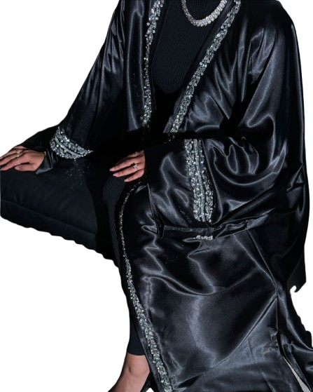 A woman in a black, high-shine satin abaya featuring heavy silver rhinestone and crystal embellishment along the front edges and wide cuffs