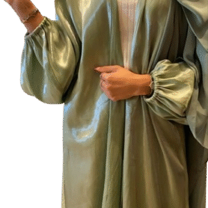 A woman in a flowing, shimmering sage green abaya with voluminous balloon sleeves, worn open over a white ribbed top and paired with a matching green hijab.