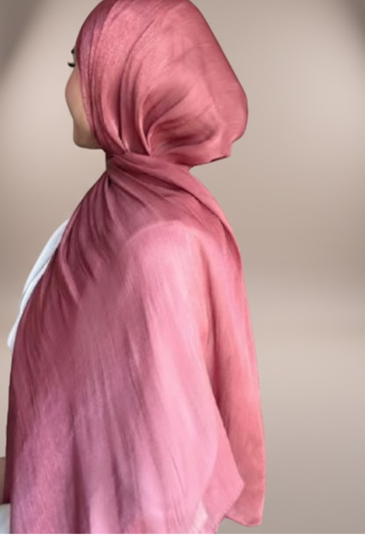 wearing a shimmery, dusty rose-colored hijab against a soft, neutral, light