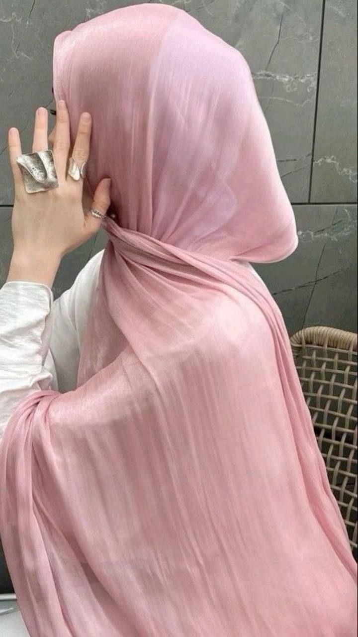 Close-up of a person wearing a pale pink, slightly shiny or crushed-effect satin hijab, elegantly draped around the neck and shoulders. The person