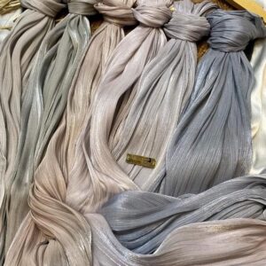 slightly shiny or crushed-effect satin hijab, elegantly draped around the neck and shoulders. The person's hand, adorned with large, textured silver rings, is visible near the chin.
