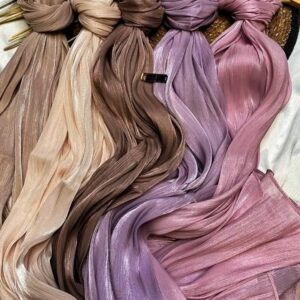 slightly shiny or crushed-effect satin hijab, elegantly draped around the neck and shoulders. The person's hand, adorned with large, textured silver rings, is visible near the chin.