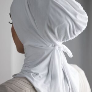 Rear view of a person wearing a close-fitting, beige/nude hijab cap/underscarf made from a soft jersey-like material, tied neatly at the nape of the neck.