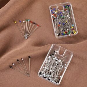 plastic cases filled with dressmaker's straight pins, one set with colorful heads and another set with black and white heads, that help to drap hijab displayed on a draped, brown/taupe chiffon-like fabric.