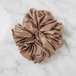 Close-up shot of a large, silky, beige/taupe satin scrunchie resting on a white and grey marble surface.