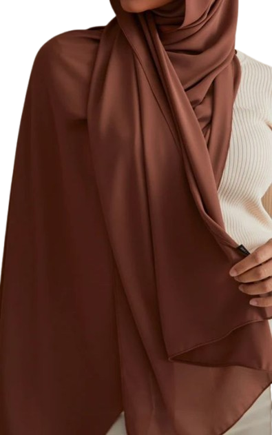 wearing a smooth, matte dark brown (chocolate) hijab draped over a ribbed, cream-colored top. A hand subtly holds the edge of the fabric.